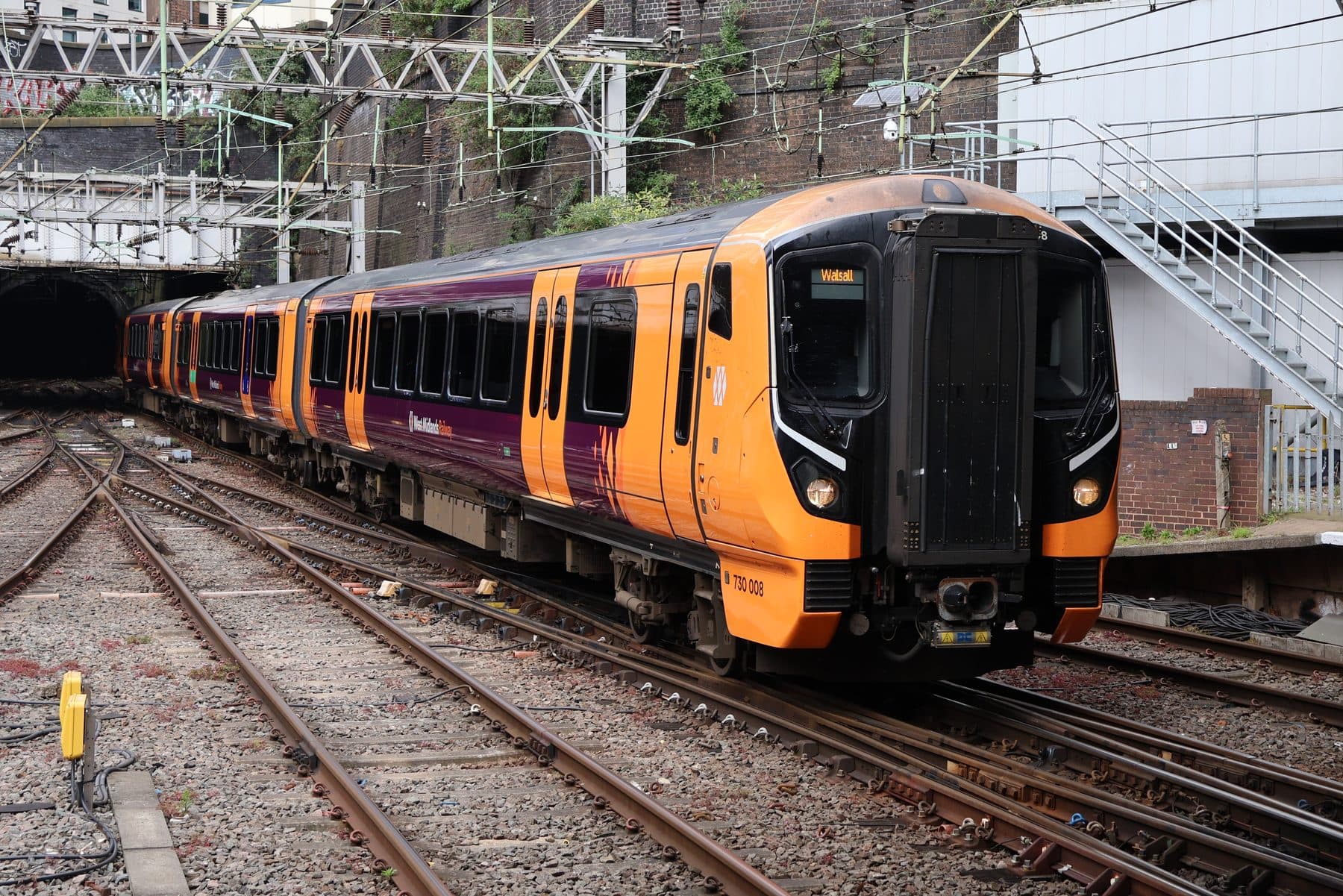 A West Midlands Railway Class 730 Aventra train in orange and purple livery arriving at Birmingham New Street